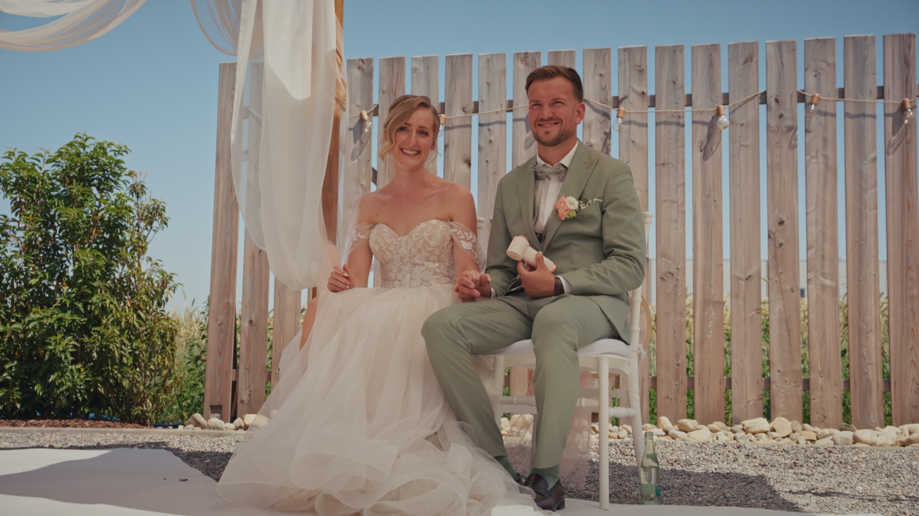 Jenny und Nico sitzen während der Zeremonie vor dem Traubogen